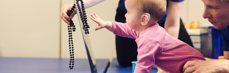 baby girl reaching out to grab beads whilst a therapist holds her legs