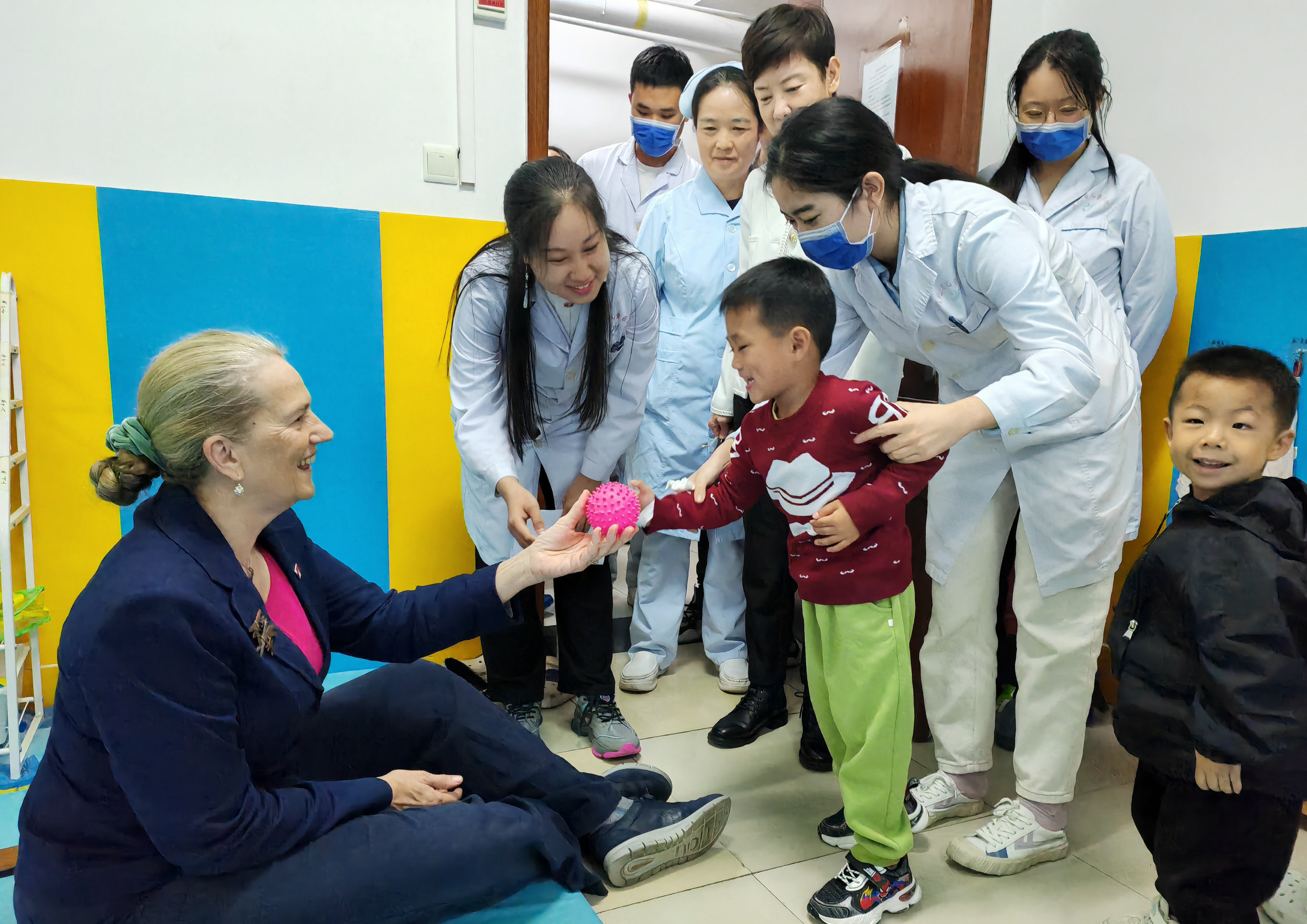Jenny pictured holding out a therapy toy to a young child, surrounded by other medical professionals.