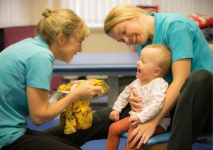 Two therapists smiling at young baby.