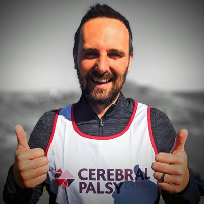 A man giving thumbs up in a Cerebral Palsy Cymru running vest.