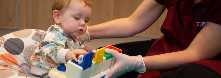 Photograph of baby playing with a therapy toy alongside therapist.