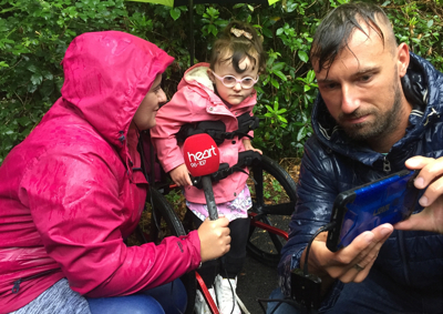 little girl in walker with mum holding a red heart radio microphone in the rain.