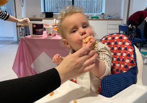 Photograph of young girl eating a cake and looking at the camera.