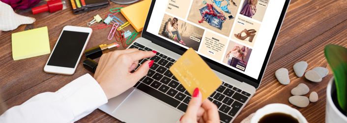 Photograph of a person doing online shopping on their laptop. One hand is holding a credit card, whilst the other hand is typing.