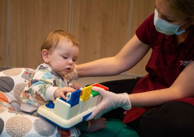 Photograph of baby looking towards, and playing with, a toy that a therapist is holding.