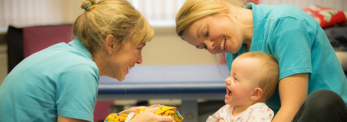 Two therapists smiling at young baby.