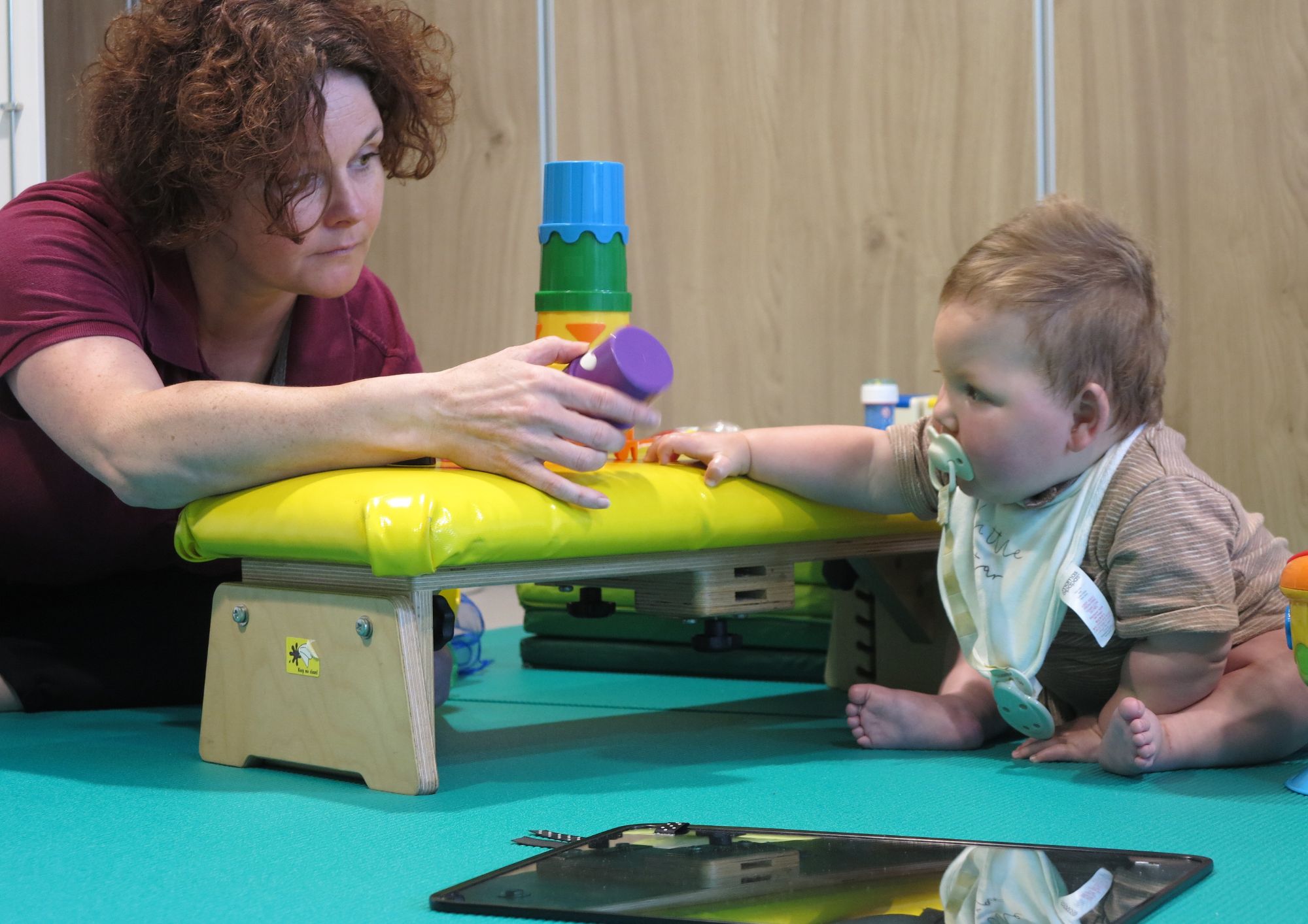 a baby reaching for a toy using a yellow therapy bench