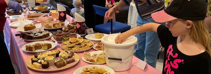 Photograph of bake sale, with young girl putting change into a bucket.