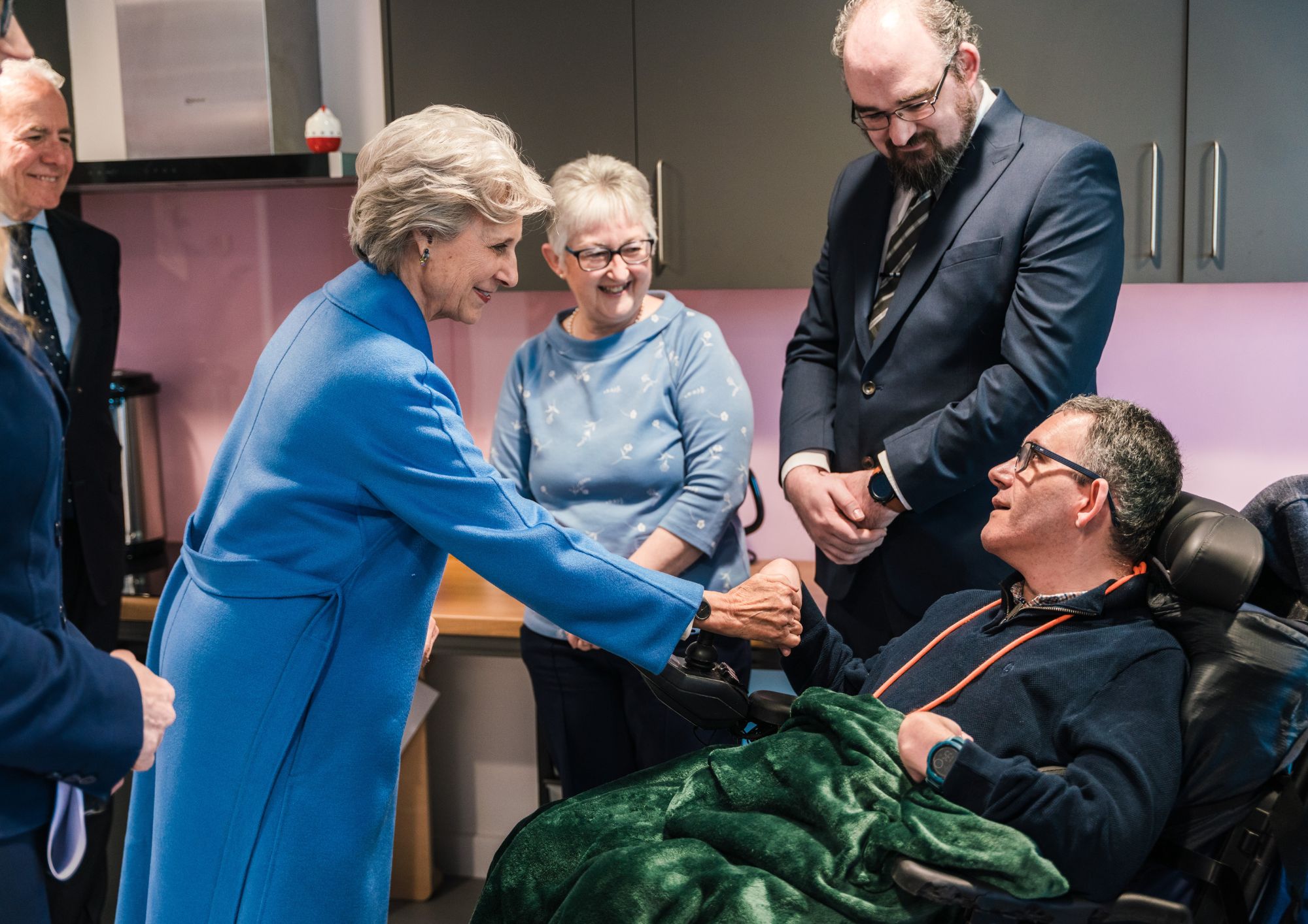 A lady in a blue coat shaking hands with a man in a wheelchair