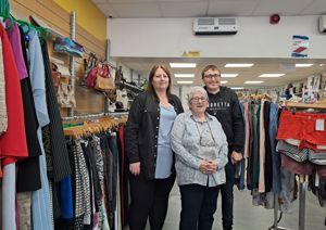 Two ladies and a young man stood in a charity shop smiling 