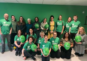 A group of men and women wearing green t-shirts and holding green balloons smiling at the camera 