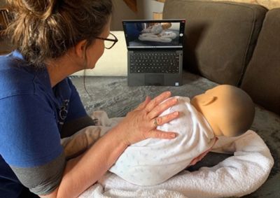 Therapist working with baby doll in front of laptop screen.
