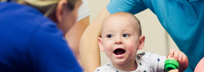 Baby with his mouth open looking towards a therapist.