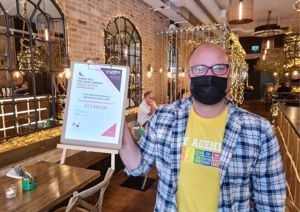 Photograph inside Mowgli Street Food Cardiff, a member of staff stands net to sign stating that they have raised over £7,4444.0.