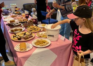 Photograph of bake sale, with young girl putting change into a bucket.