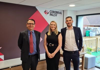 Photograph of three Harding Evans Solicitors standing in front of our Cerebral Palsy Cymru branded wall in our centre.
