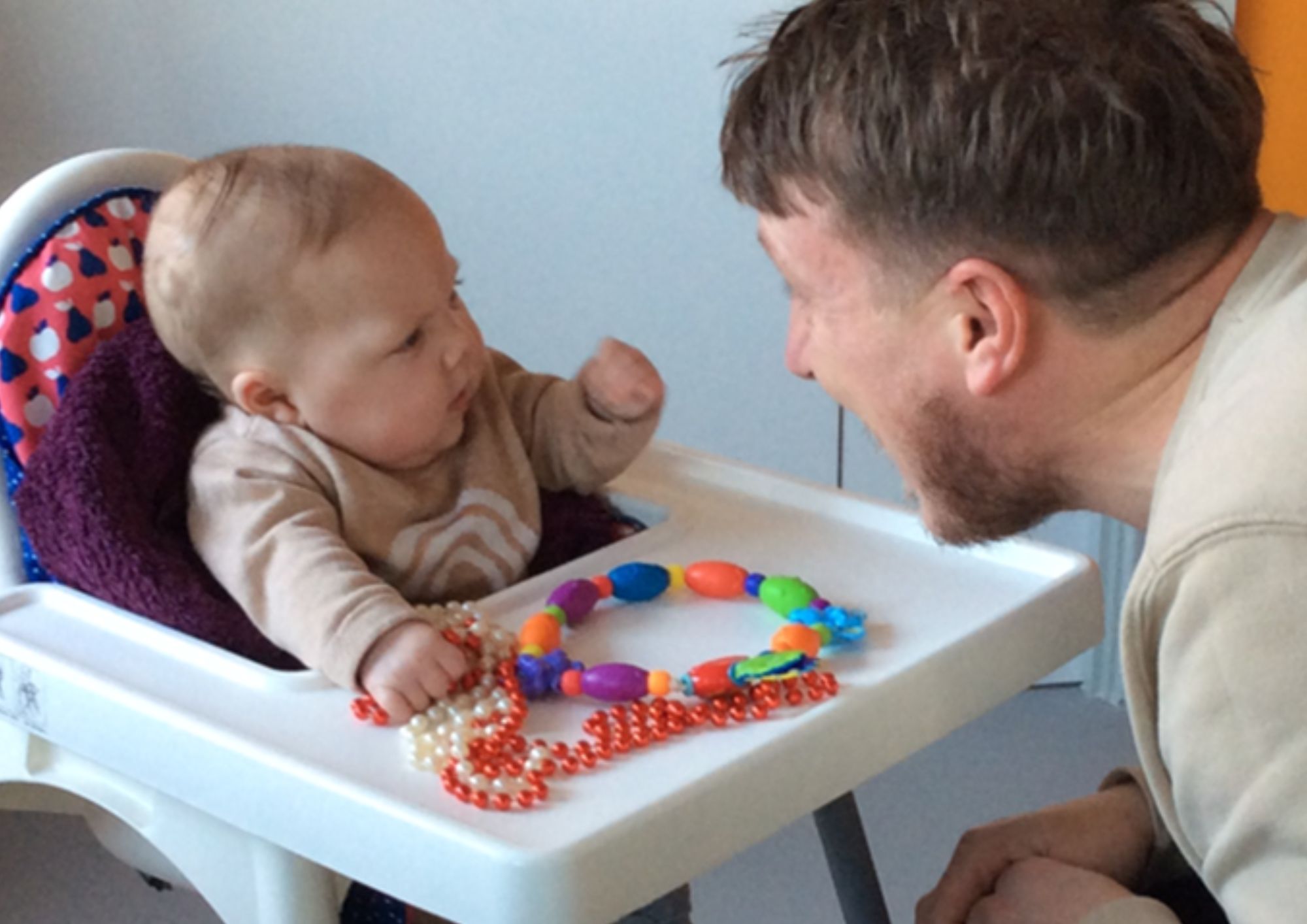 a baby in a high chair looking at his dad who is smiling at him