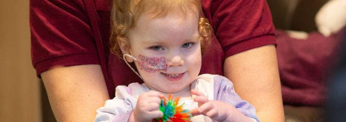 Photograph of young girl smiling at camera whilst holding a therapy toy.