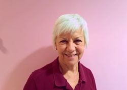 A photograph of our Speech and Language Therapist and Lead for Clinical Effectiveness in front of our pink wall.