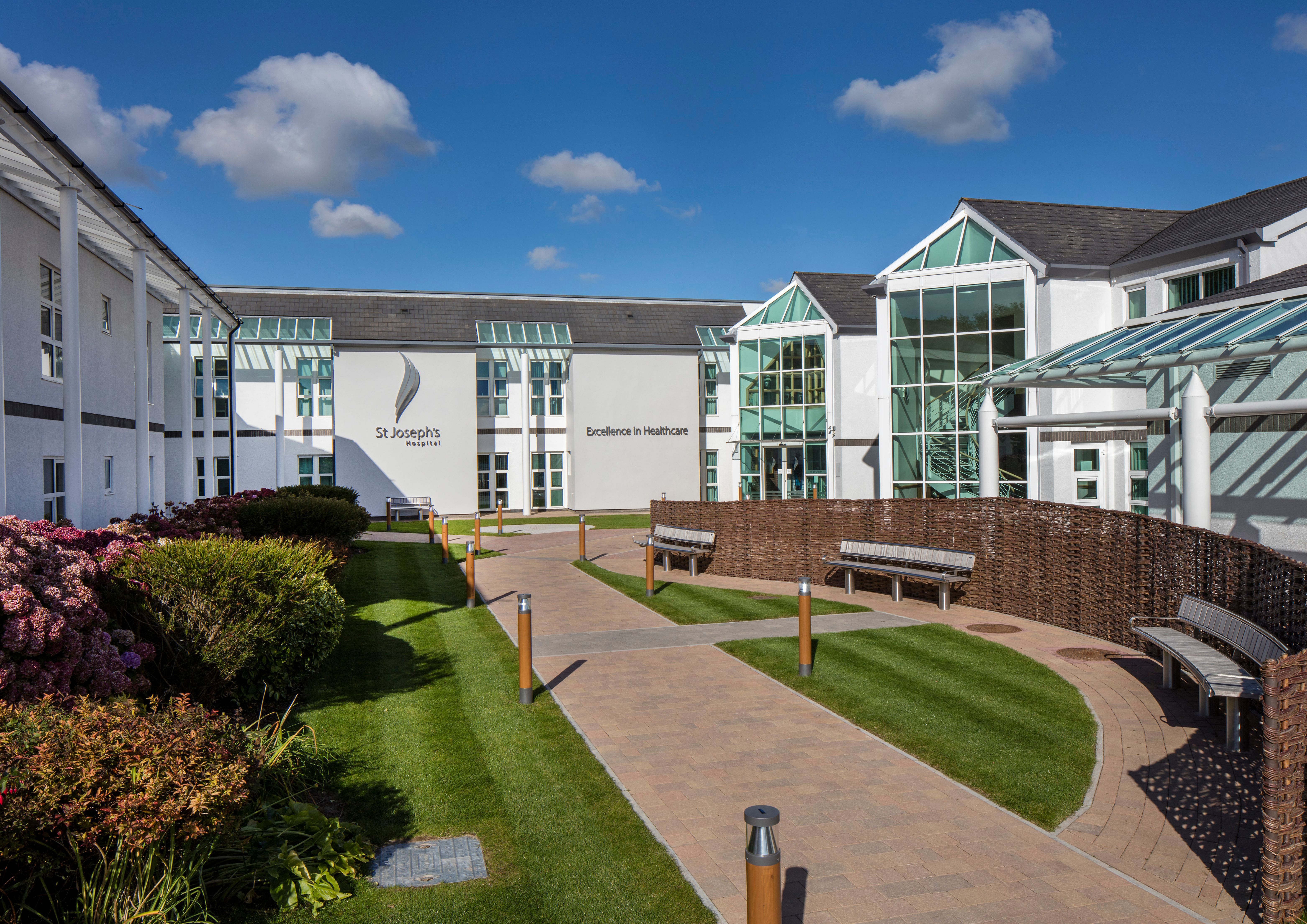 Photograph of the outside of the St Joseph's hospital building, including a green space with benches.