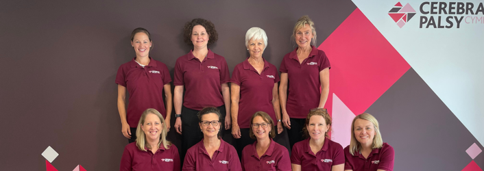 Photograph of therapy team (9 women) some seated, some standing, in front of Cerebral Palsy Cymru branded wall in our centre. 