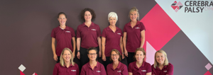 Photograph of therapy team (9 women) some seated, some standing, in front of Cerebral Palsy Cymru branded wall in our centre. 