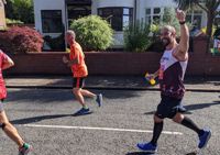 Photograph of Gareth, in his Cerebral Palsy Cymru running vest, running the Cardiff Half and waving at the camera.