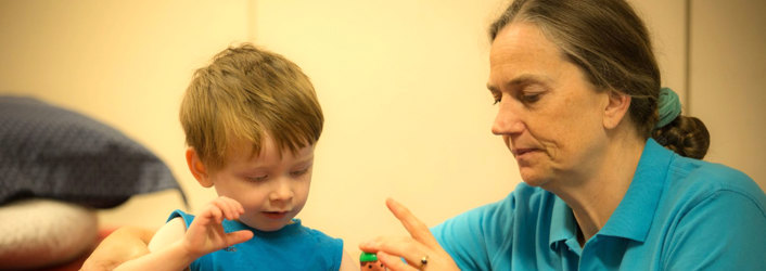 Young boy playing with therapy toy that therapist is holding.