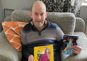 Photograph of Gavin Clifton seated, holding up two of his books titled 'Max and the Magic Wish' and 'Lola'.