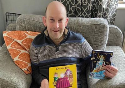 Photograph of Gavin Clifton seated, holding up two of his books titled 'Max and the Magic Wish' and 'Lola'.