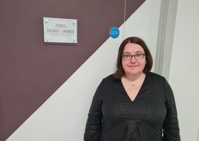 Photograph of female Hugh James lawyer standing in front of Hugh James plaque in our centre.