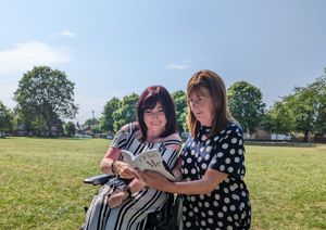 Photograph of Samantha Maxwell, alongside Lesley Griffiths with grass in the background. Both women are looking at the book 'CP Isn't me' which Lesley is holding out open in front of them.