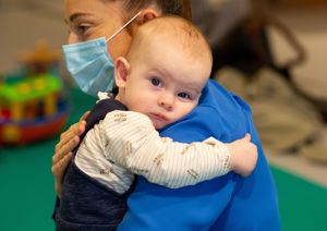 Photograph of baby being held by mother, looking into the camera.