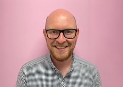 Photograph of of Head of retail in front of our pink wall.