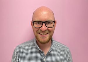 Photograph of of Head of retail in front of our pink wall.