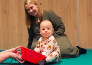 A baby sat on a therapy mat playing with a red plastic bowl