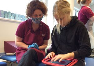Photograph of a therapist and a young woman looking down towards an ipad. 