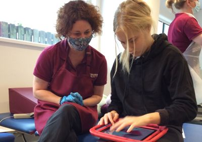 Photograph of a therapist and a young woman looking down towards an ipad. 
