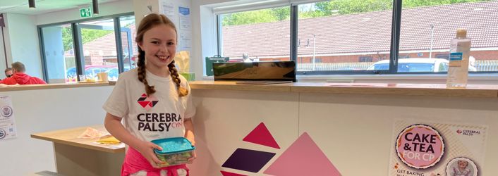 Photograph of young girl in Cerebral Palsy Cymru t-shirt, holding a box of cakes. 