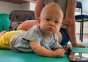 Photograph of baby boy lying on his front, looking up at the camera.